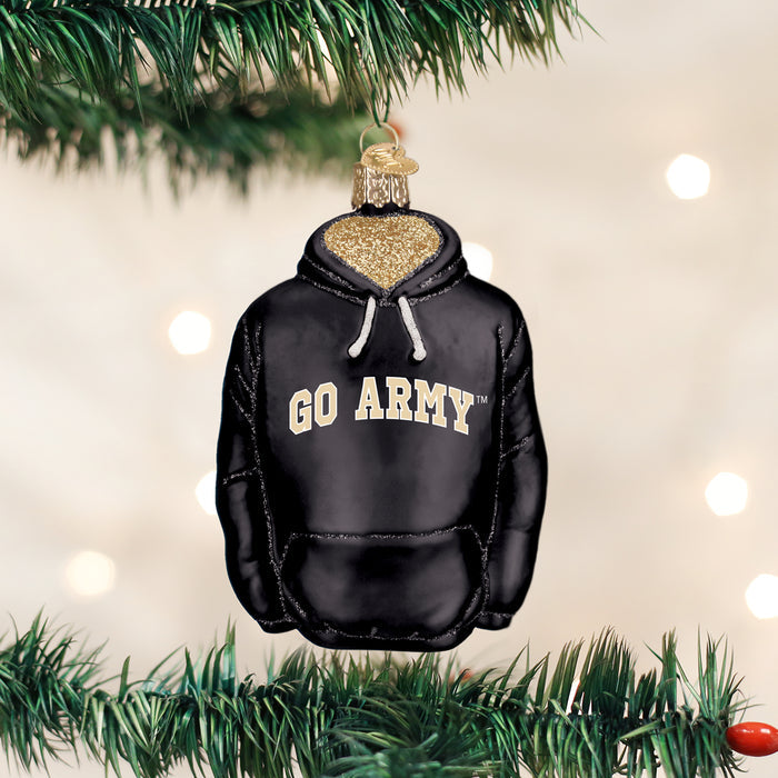 A Christmas tree ornament shaped like a black hoodie with â€œGO ARMYâ€_x009d_ written on the front hangs on a green pine branch, with soft white lights blurred in the background.