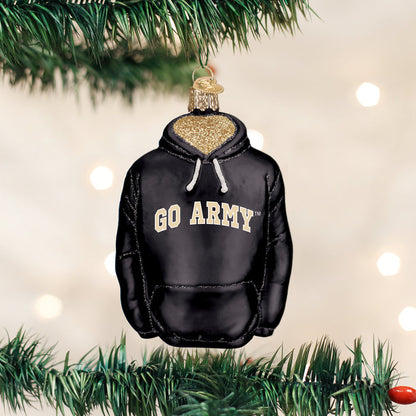 A Christmas tree ornament shaped like a black hoodie with â€œGO ARMYâ€_x009d_ written on the front hangs on a green pine branch, with soft white lights blurred in the background.