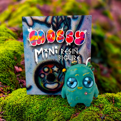 Mossy - The Mini Moss Spirit by Mumbot, a small resin toy depicting a forest spirit, sits on moss, emphasizing its whimsical and artistic design.